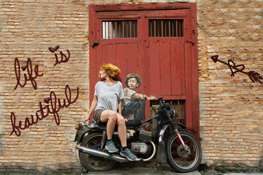 Girl and boy sitting on motorbike in front of brick wall